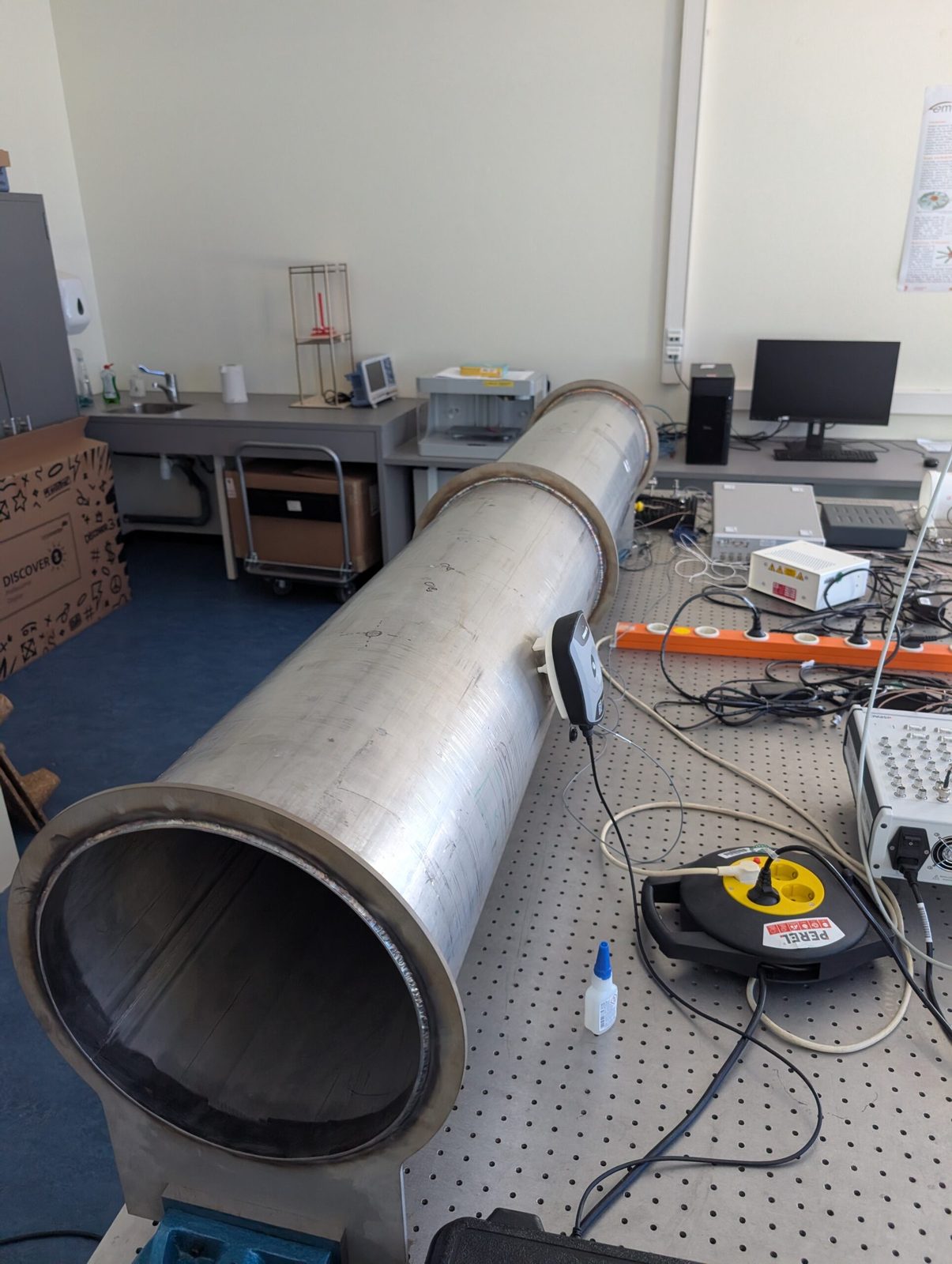 A steel tube section on an optical table with a vibration sensor fixed to its shell
