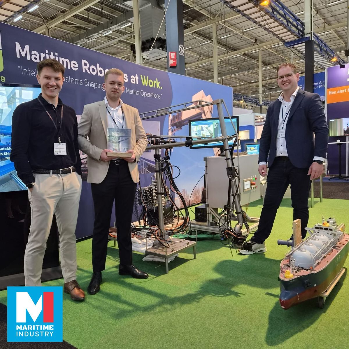 Three men at the AutoMooring Solutions stand beside a robotic mooring arm and a scale model of an LNG carrier, one holding an award