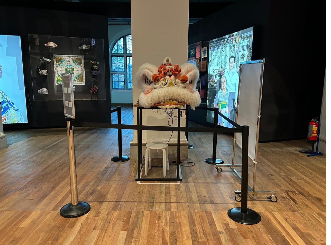 The robotic lion head head-on behind stanchion barriers in the museum gallery