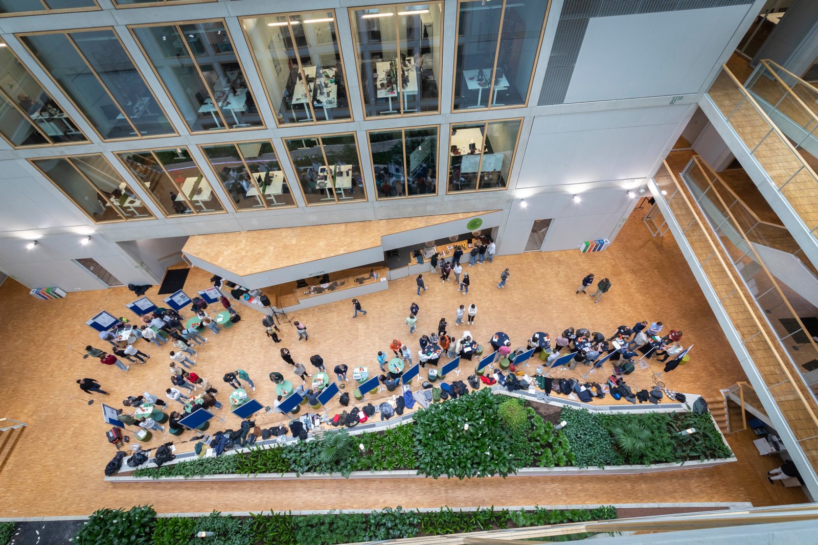 A university atrium seen from a high balcony, filled with poster boards, tables and visitors