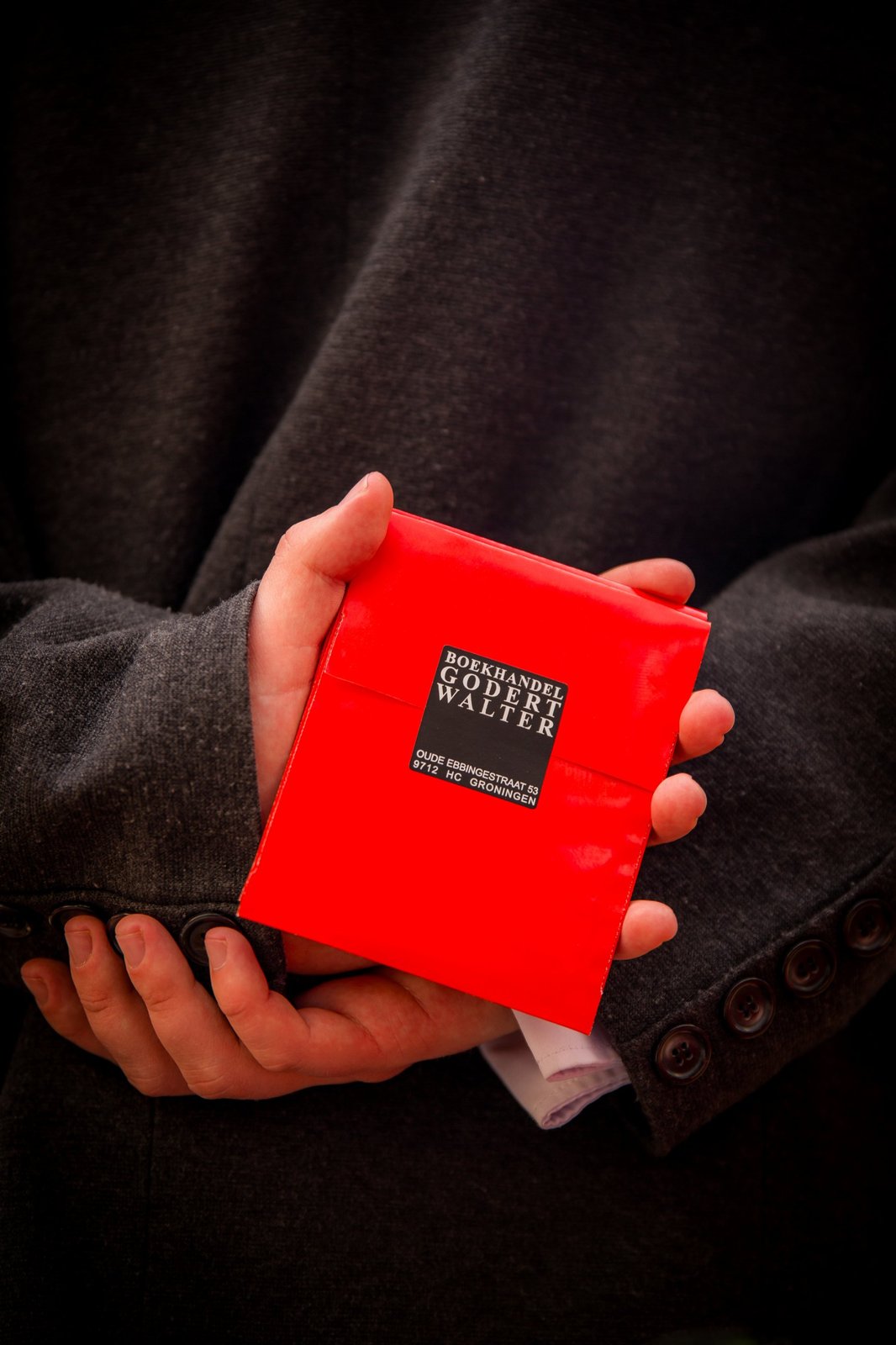 Hands behind a dark jacket holding a small red parcel from a Groningen bookshop