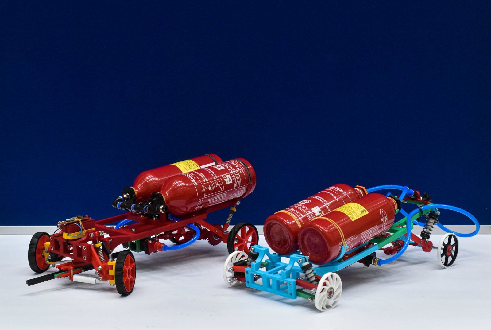 Two printed rovers, one red and one blue and green, each carrying two red air bottles linked by blue tubing, against a dark blue backdrop