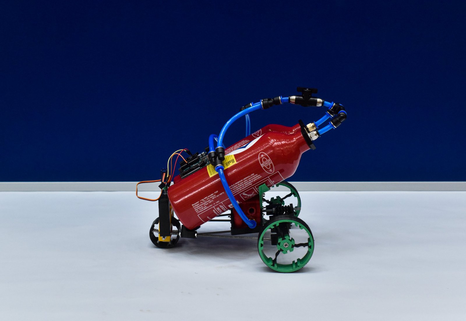 A small rover with green wheels carrying a red air bottle at an angle, blue tubing and a microcontroller board