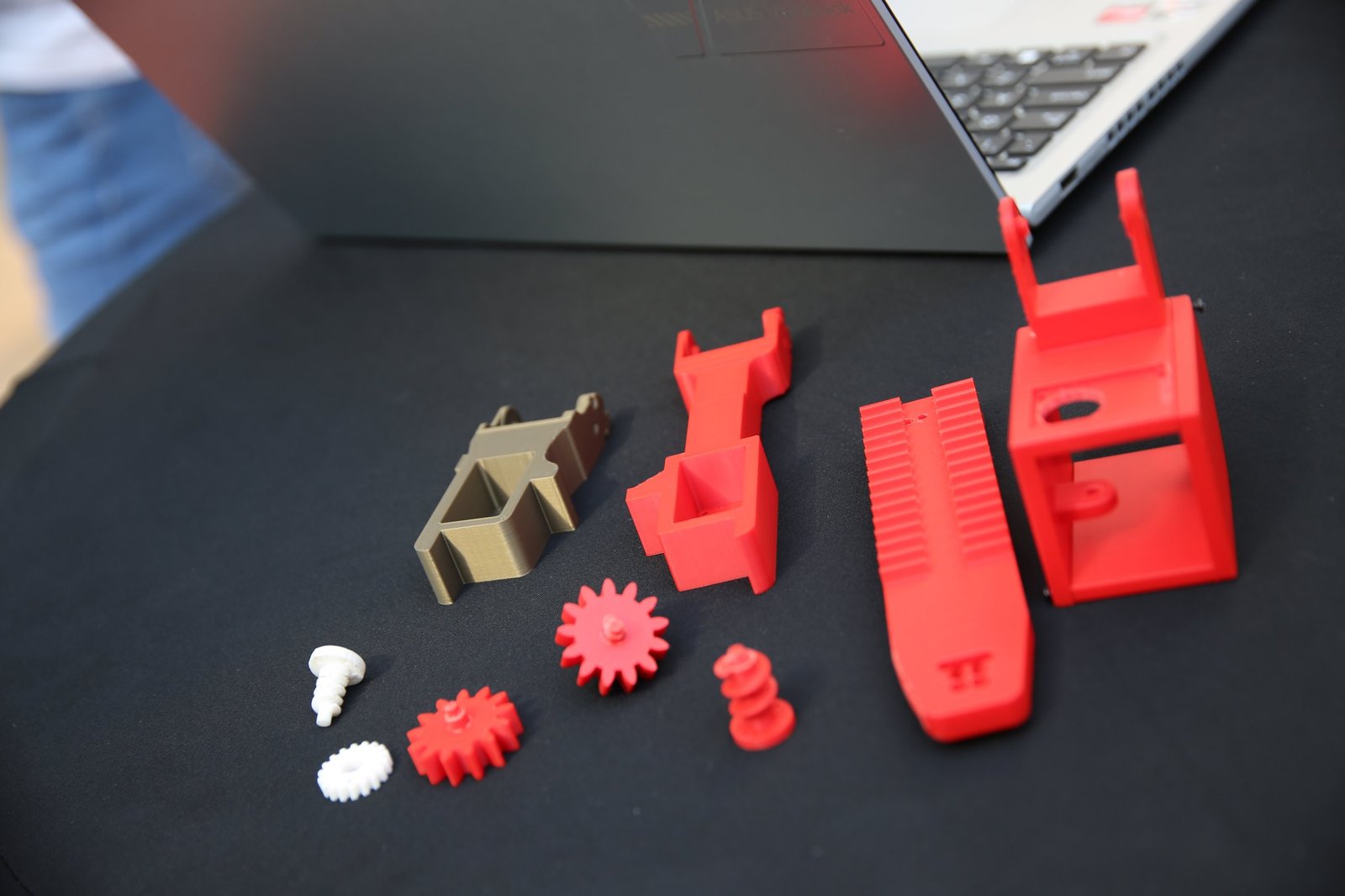 Printed parts laid out on a black table: brackets, a toothed rack, spur gears and printed screws