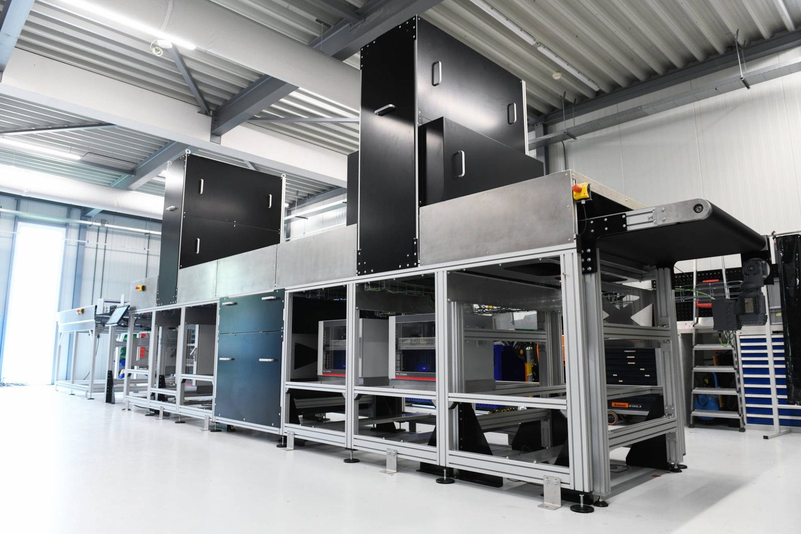 A long prototype sorting machine with black sensor housings above a conveyor belt, in a white hall
