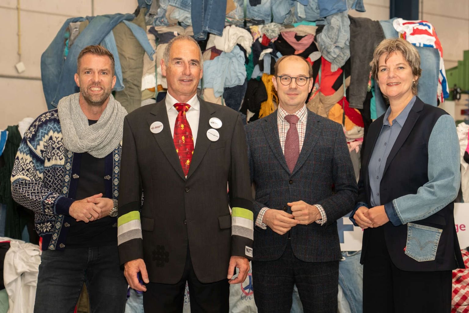 Four people standing in front of a wall of baled used clothing